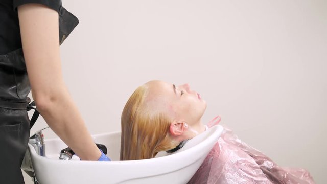 A close up side view of the hairdresser holding a shower and washing blonde's hair in the backwash basin.