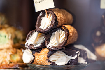 Closeup of chocolate cannoli stuffed with cream cheese whipped filling dessert on glass plate window display in gourmet bakery Italian cafe with golden crust, cannolo sign - obrazy, fototapety, plakaty