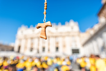 Macro closeup of wooden olive tree handmade Italian cross Catholic rosary with bokeh background of Vatican church St Peter's Square Basilica during mass on sunny summer day