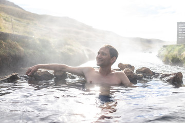 Young happy man swimming bathing in Hveragerdi Hot Springs on trail in Reykjadalur, during autumn summer morning day in south Iceland, golden circle, rocks and river steam