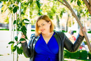   Portrait of plus size girl in blue dress and leather jacket in the park