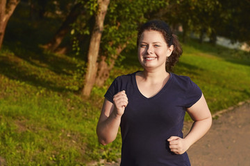 Happy plump girl run in forest and smiling. Overweight woman jog in park.