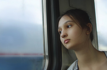 Fototapeta na wymiar A sad young girl rides a train and looks out the window.