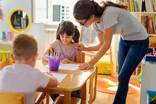 Preschool teacher assisting children with their drawings. Early education. Harnessing creativity and support.