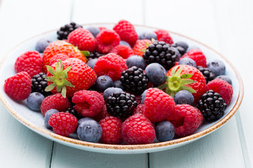 Fresh berry salad on blue dishes. Vintage wooden background.