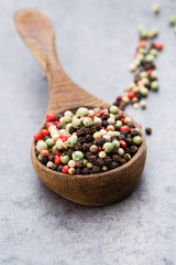 Peppercorn mix in a wooden bowl on grey table.