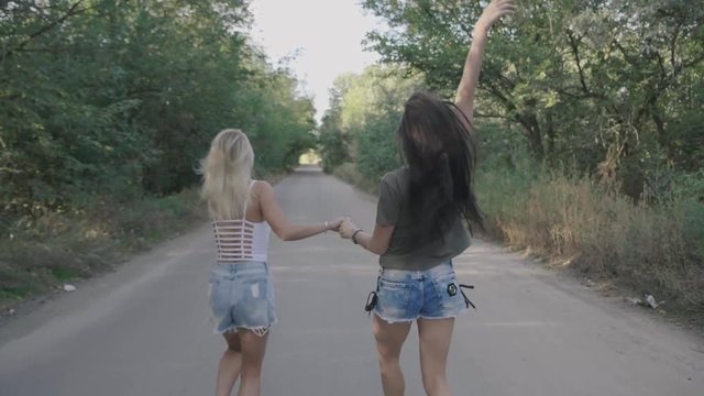 Two best friends sexy hot girls runnung and having fun together on a road at forest or park.