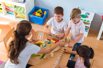 Preschool teacher with children playing with colorful wooden didactic toys at kindergarten