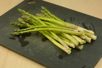 Bunch of freshly rinsed whole raw asparagus spears on black cutting board