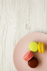 Colorful macaroons on a pink plate over white wooden surface, top view. Close-up.