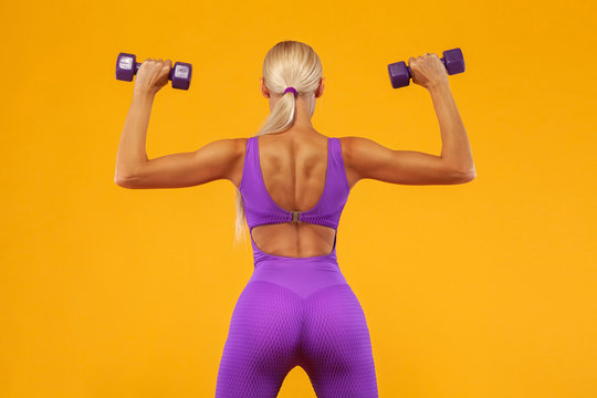 Fitness woman athlete and bodybuilder holding dumbbell . Isolated on yellow background. © Mike Orlov