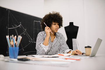 Stylish African American hipster freelancer researching information online using laptop computer...