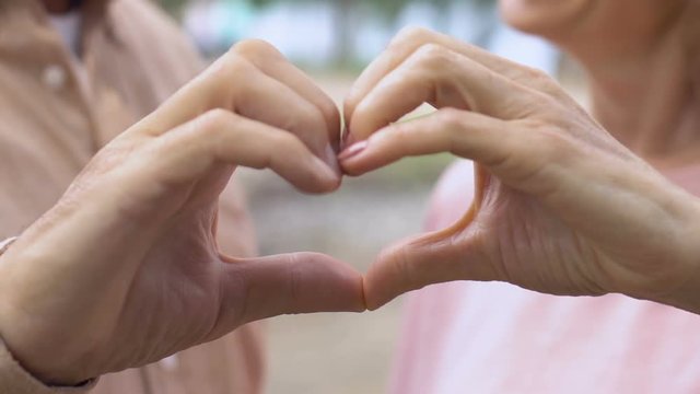Mature man and woman showing heart sign with their fingers, sweet love, close up