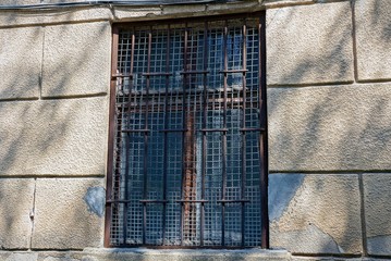 one old brown window behind bars on a gray concrete wall of a building