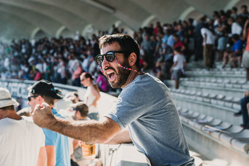 .Young man enjoying a rugby match at the stadium on a sunny autumn day. Screaming, celebrating and encouraging your team. Lifestyle. - obrazy, fototapety, plakaty