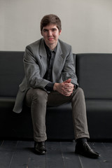 Handsome young man in suit sitting on couch in reception. Business man waiting for meeting.