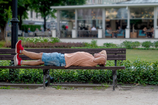 A middle age man lying on a bench in the park.