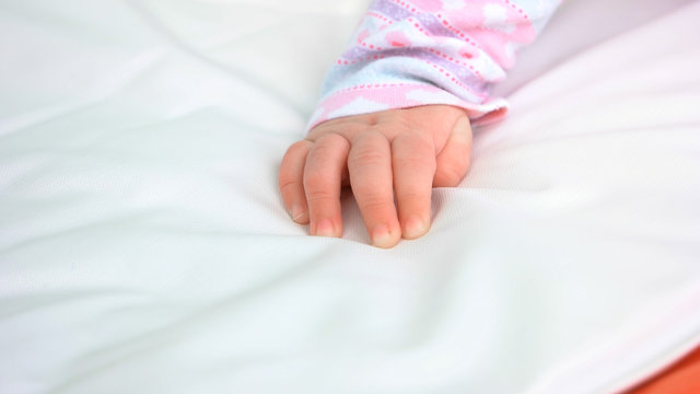 Hand of infant baby girl. Hand of newborn caucasian kid on white blanket. Softness of skin.