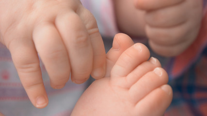 Obraz na płótnie Canvas Close up hand and leg of infant baby. Hand of infant plays with feet close up. Baby care concept.