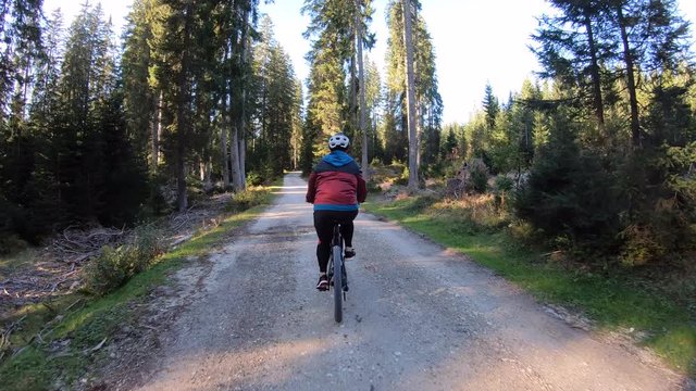 Tracking shot. Woman riding mountain bike on a gravel forest road