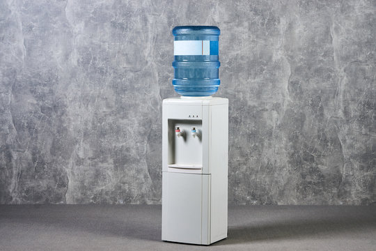 White water cooler gallon in office against gray textured wall background. International Exhibition furniture elements in large warehouse interior.
