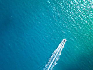 Bird's eye aerial top view of a boat cruising in crystal clear turquoise sea water