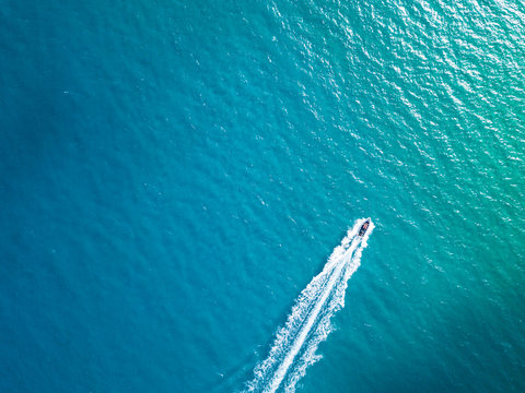 Bird's eye aerial top view of a boat cruising in crystal clear turquoise sea water