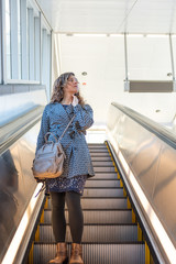 Low angle view, looking up, portrait of young woman standing on metro, subway, airport escalator going down with stairs, steps, bright light outside