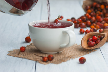 Dried rose hip cup of herbal tea medicinal plants on white black wooden table with wooden shovel and rosehips in burlap sack. Dogrose background