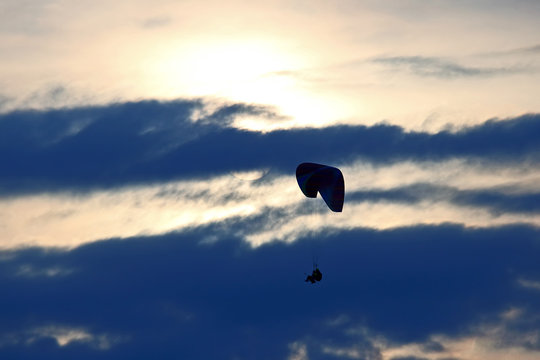 Paraglider flying on a wing in the sky against the setting sun