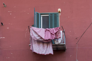 Pink washing drying on a balcony outside a window with green shutters on streets of Naples Italy