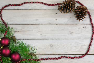 Scotch pine boughs and pine cones on whitewashed boards with a border of cranberry beads and 3 ornaments