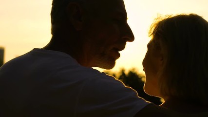 Old man saying compliment to woman and hugging her on romantic date outdoors