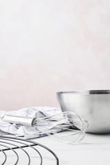 Baking concept. Bowl with a whisk, dishcloth and French wire rack on white marble table over pink background with copy space.