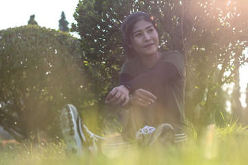 Woman sitting under a bush on a lawn.