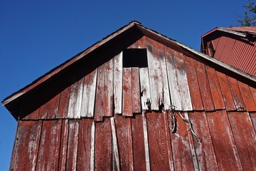 Fototapeta na wymiar Pocono Mountains, Pennsylvania, USA: The peak of an abandoned barn with peeling red paint against a deep blue sky.