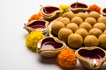 Diwali Rangoli using Diya, flowers and Besan Laddu or Laddoo arrabged over white background, selective focus