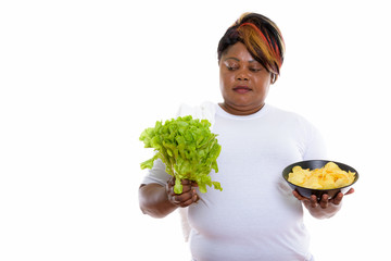 Studio shot of fat black African woman looking at lettuce and ho