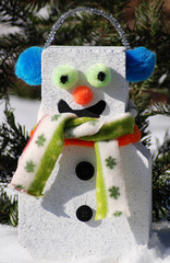 Comical brick snowman with multicolored scarf and blue earmuffs in snow