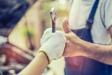 Mechanic hand checking and fixing a broken car in  garage.hand of mechanic with thumbs up and tool