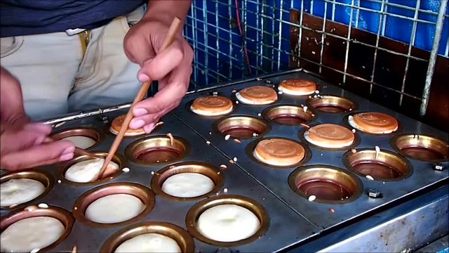 A food vendor cooks mini pancakes on a food cart.