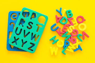 Alphabet for kids concept. English letters in disorder near stencil on yellow background top view