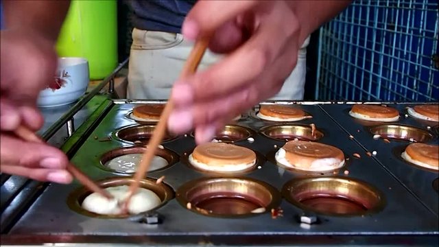 A food vendor cooks mini pancakes on a food cart.