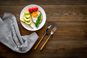 Recipe of fried eggs for vegetarian breakfast. Fried eggs with cherry tomatoes and greenery near toast with avocado on dark wooden background top view copy space