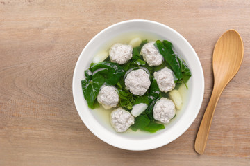 top view of pork ball clear soup with ivy gourd in a ceramic bowl on wooden table. homemade style healthy food concept.