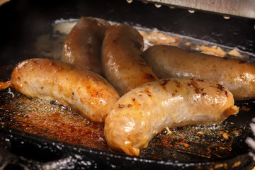 Sausages are fried in boiling oil in a hot frying pan. Close-up