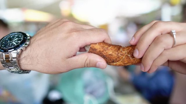 Two people are splitting a bagel in to two pieces