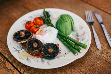 breakfast of poached egg, mushrooms, avocado and tomato asparagus in a plate on wooden table.