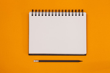 Blank spiral notebook and pencil on orange background. Top view with copy space for input the text. - obrazy, fototapety, plakaty
