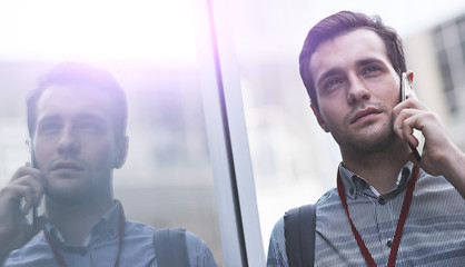 successful young man talking on the phone against a reflective wall background